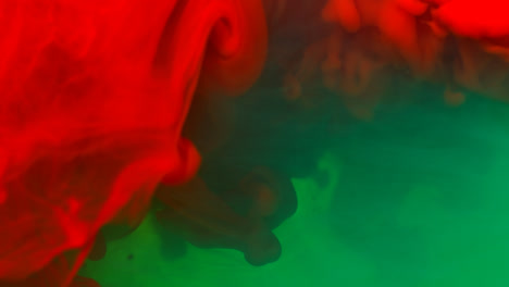 Green-And-Red-Paint-Or-Dye-Dropped-Into-Water-Against-White-Background-To-Create-Swirling-Colourful-Smoke-Background